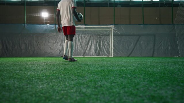 Black soccer player exercising penalty in training hall, scoring goal, back view
