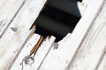 Close-up of Weathered Wooden Deck with Large Hole, Damaged Boards, and Peeling Paint in Sunny...