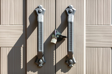 Locked wooden doors with metal handles and keys hanging on padlock in sunlight, symbolizing...