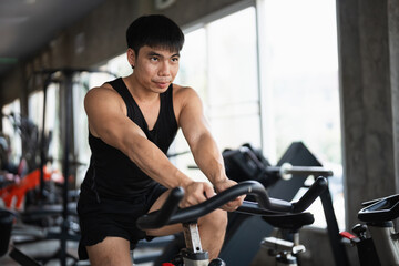 A determined man in a black tank top performs a cycling workout on a stationary bike in a modern...