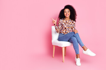 Full length photo of adorable lovely girl wear print shirt sitting stool pointing empty space isolated pink color background