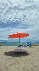 Beautiful tropical scenery, two sun beds and orange umbrella. White sand, blue sky clouds at Mui Nai beach, Ha Tien, Vietnam in summer.