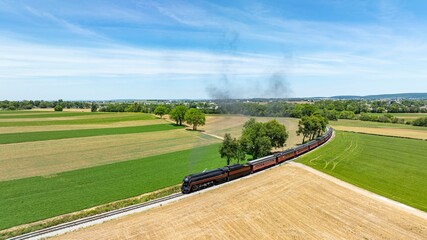 A captivating aerial shot of a steam train gliding through a green rural panorama, weaving between...