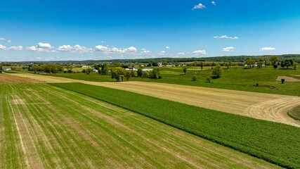 A striking aerial photograph capturing a tapestry of agricultural fields, each with different textures and shades of green and gold, under a sky with scattered clouds, providing a broad view of rural
