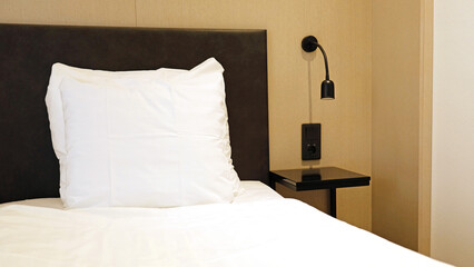Modern bed​room interior​ design home or hotel. Fragment of bedroom with empty bedside table, reading lamp and socket for charging gadgets. Soft pillow and blanket, stylish comfortable furniture.