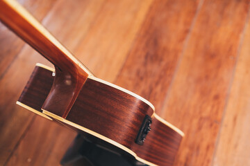 Top and semi-back view of six strings acoustic guitar on stand support on wooden floor. Selective focus. Copy space.