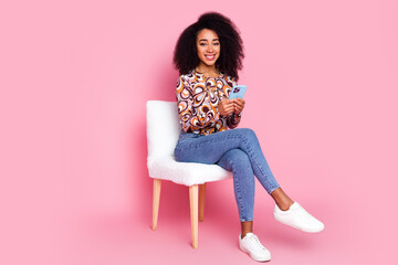 Full length photo of charming girly woman wear print shirt sitting stool texting modern gadget...