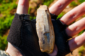 A stone tool covered with a whitish patina lying on the palm, an ancient Stone Age artifact at the...