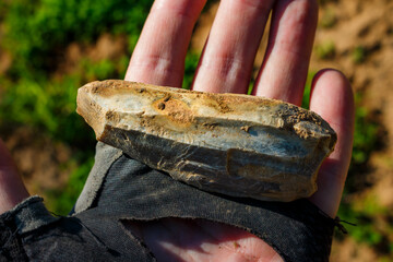 A stone tool covered with a whitish patina lying on the palm, an ancient Stone Age artifact at the discovery site, Russia