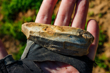 A stone tool covered with a whitish patina lying on the palm, an ancient Stone Age artifact at the...