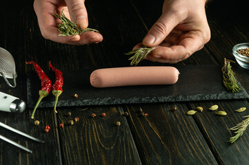 Vedeno sausage on a serving board. The chef hands add fragrant rosemary to the sausage before...