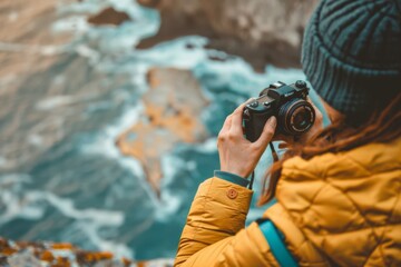 Obraz premium A woman in a hat takes a photo of the ocean on rocky shore