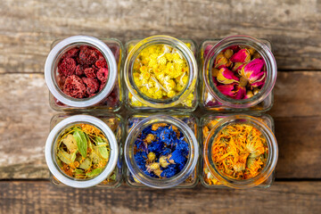 Assortment of dry herbal and berry tea in glass jars on a wooden background.Medicinal Healing herbs.Alternative medicine concept.Linden, calendula, cornflowers, marigold, tansy, tea rose.dry herbal