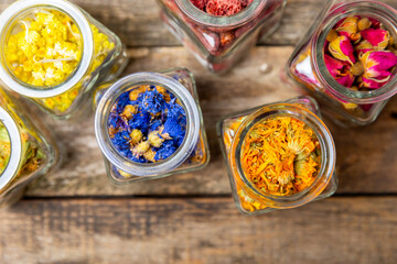 Assortment of dry herbal and berry tea in glass jars on a wooden background.Medicinal Healing herbs.Alternative medicine concept.Linden, calendula, cornflowers, marigold, tansy, tea rose.dry herbal
