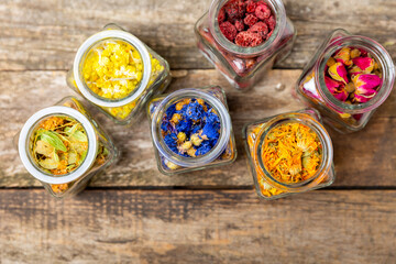 Assortment of dry herbal and berry tea in glass jars on a wooden background.Medicinal Healing herbs.Alternative medicine concept.Linden, calendula, cornflowers, marigold, tansy, tea rose.dry herbal