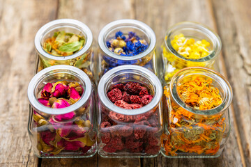 Assortment of dry herbal and berry tea in glass jars on a wooden background.Medicinal Healing herbs.Alternative medicine concept.Linden, calendula, cornflowers, marigold, tansy, tea rose.dry herbal