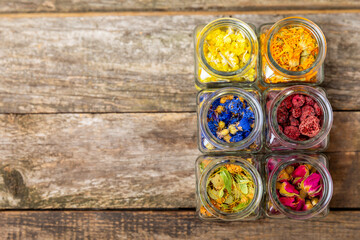 Assortment of dry herbal and berry tea in glass jars on a wooden background.Medicinal Healing herbs.Alternative medicine concept.Linden, calendula, cornflowers, marigold, tansy, tea rose.dry herbal
