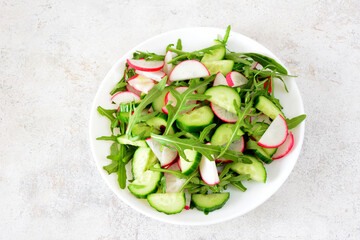 a plate of salad with radish, cucumber and arugula leaves top view