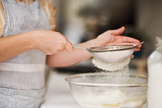 Woman, hands and sifting flour in kitchen for cookies, bread and breakfast ingredients in cafe. Female baker, cooking and dessert for bakery, small business and startup coffee shop or restaurant