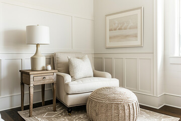 A clean, simple room with an armchair and ottoman in neutral tones,complemented by white wainscoting and wall art. The lighting is soft, creating a cozy atmosphere.A small wooden side table next to it