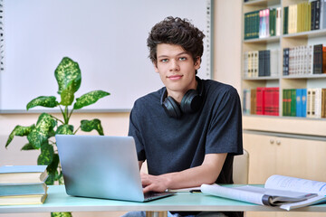Portrait of college student guy sitting at desk with laptop inside an educational library