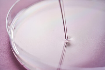 Serum or cosmetic oil flows into a transparent bowl on a purple background.