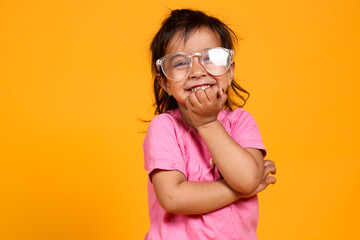 A young child with a bright smile , The child is wearing a pink shirt and large, clear-rimmed...