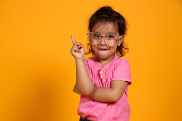 A young child with a confident smile stands against a vibrant orange background. The child is...
