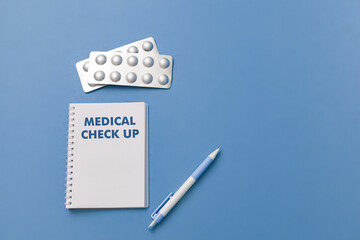 Medical check up concept on blue background: Notebook, medicine, pen and medical tools symbolizing healthcare examination.