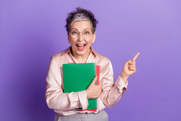 Photo portrait of lovely senior lady point empty space hold papers dressed stylish satin garment isolated on violet color background