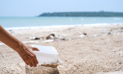 Woman hands pick up plastic food box left on the sandy beach, Cleaning the beach, Collecting trash at the beach. Environmental Conservation concept.