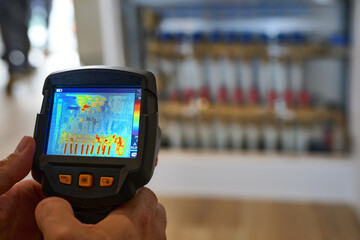 The image depicts a handheld thermal camera being used to measure the temperature of an underfloor...