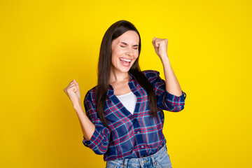 Photo portrait of attractive young woman winning raise fists dressed stylish plaid clothes isolated on yellow color background