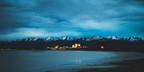 Wide shot of a golden city at dusk  by the ocean with mountains surrounding behind, anchorage alaska