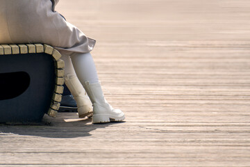 Girl's legs in white high-top boots, seated on a bench