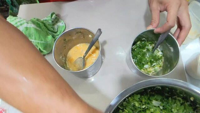 High angle shot of hands adding some of onion leaves cuts into stirred egg yolk. Preparing to cook an omelette. Perfect for culinary projects or tutorials