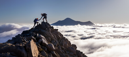 Silhouettes of two people climbing to summit of mountain, helping each other, offering a helping hand. Teamwork and 
