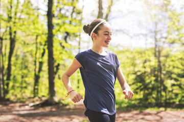 Fit child girl jogging in green park on a sunny summer evening.