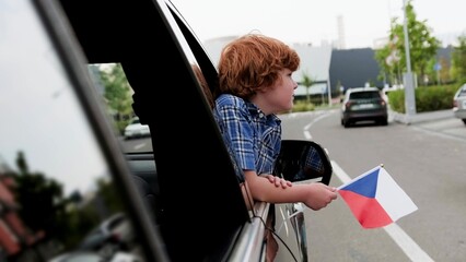 Child traveling in Czech, showing flag, looking out the car window. Trip, lifestyle concept.