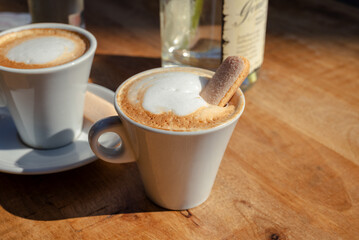 Drinking a cup of cappuccino on the terrace in the sunshine with a ladyfinger biscuit cookie. 