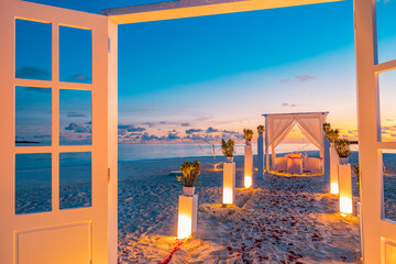 Amazing romantic dinner on colorful sunset beach. Wooden door wedding decoration candles under...