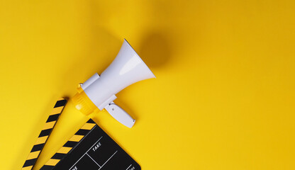 Clapper board in yellow and black with megaphone on yellow background.