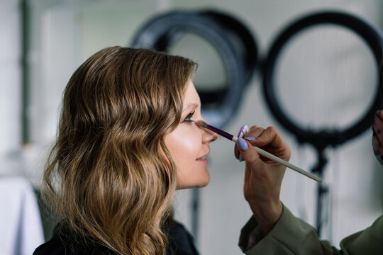 Backstage of the photo shoot: Make-up artist applies makeup on beautiful white model.