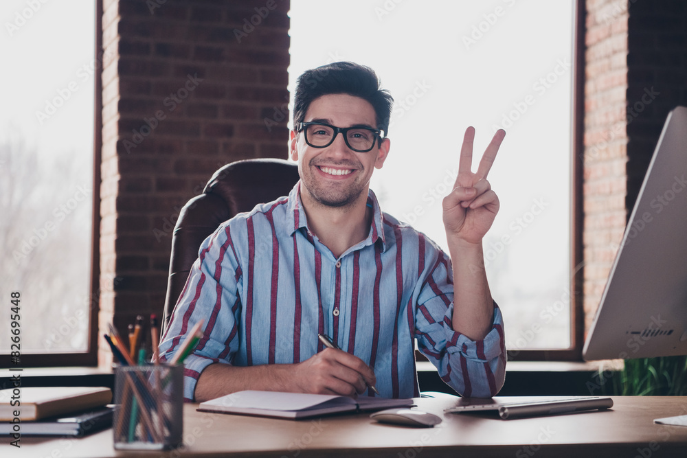 Wall mural Photo of young man corporate worker demonstrate v-sign wear striped shirt modern office home indoors