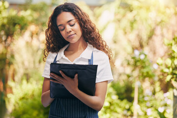 Woman, florist and writing on clipboard in garden for stock, plants or sustainable growth at store. Person, checklist and check stats with notes, ideas or progress with review at eco friendly nursery