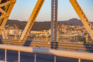 a lua perto do pôr-do-sol e a estrutura da  ponte Hercílio Luz emoldurando parte da cidade de ...