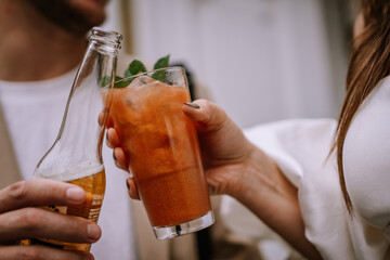 Riga, Latvia, - August 26, 2023 - Close-up of two people toasting with a beer bottle and a cocktail, showing hands holding the drinks...
