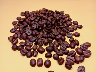Spilled coffee beans on a yellow background. Heap of roasted coffee beans isolated on yellow background. Popular drinks that cause habit. Grains that contain caffeine.