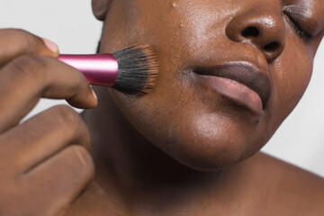 Brown skinned woman applying foundation with makeup brush, dark skin woman using a stippling brush...