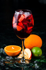 Sangria in glass with orange, lemon and apple, dark background